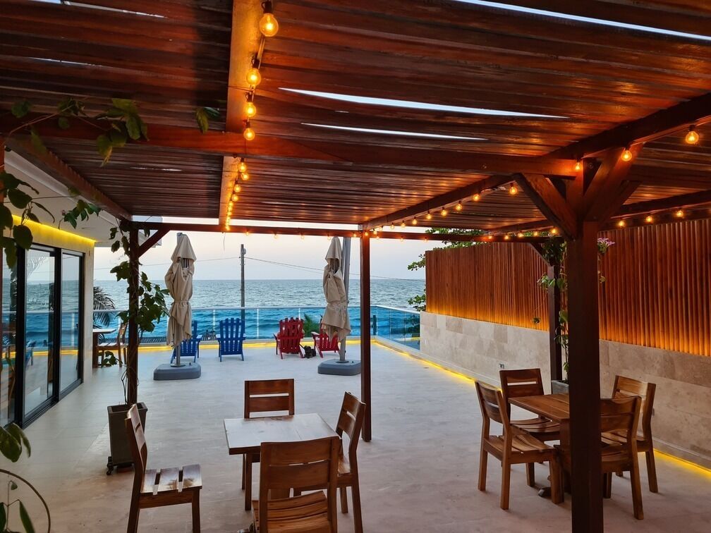 An outdoor patio with wooden tables and chairs, overlooking the ocean.