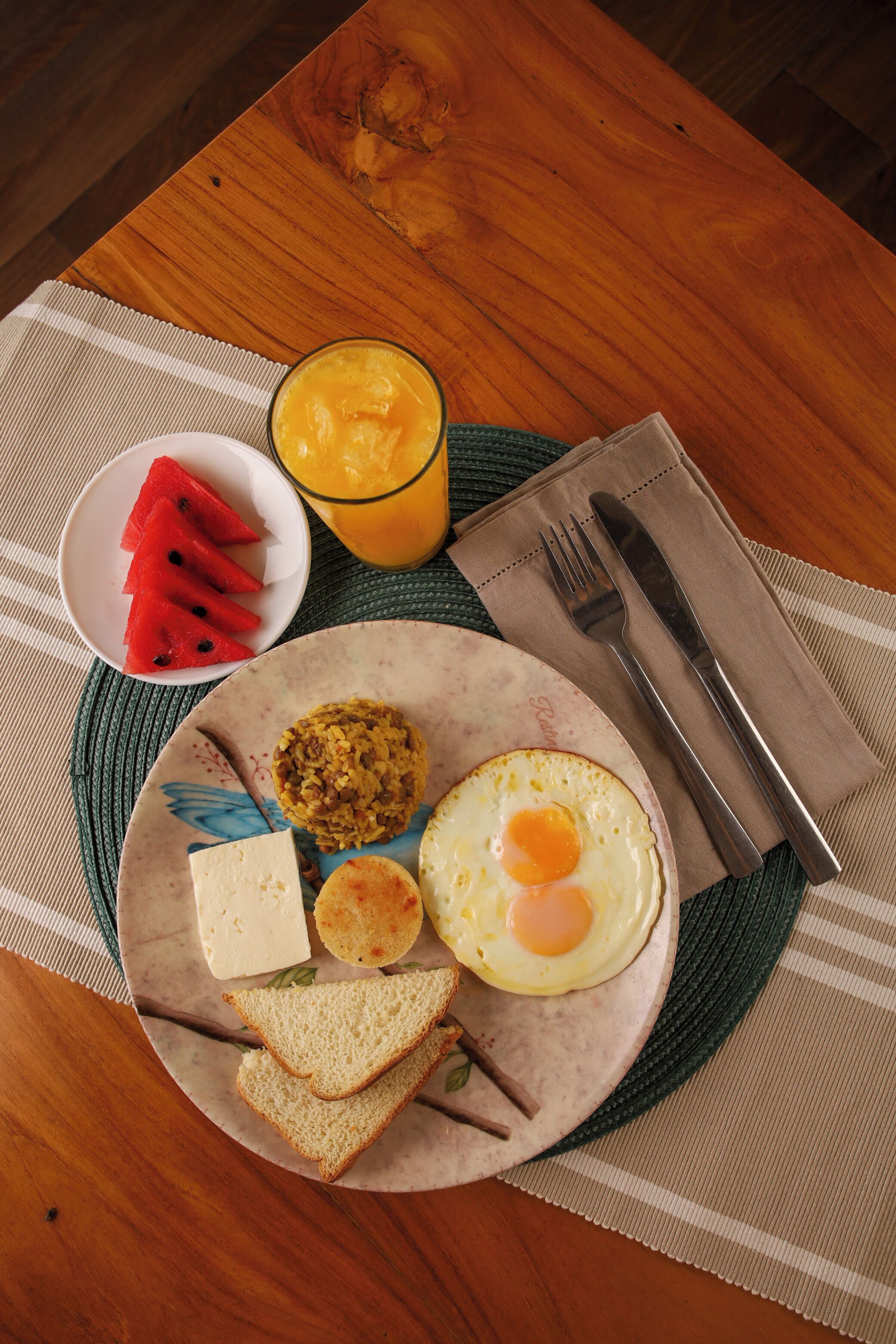 A plate with a fried egg, toast, cheese, and a fruit salad on a wooden table.