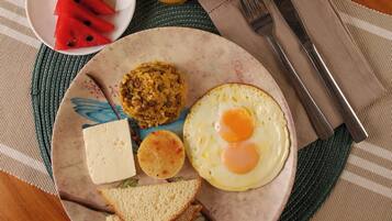 A plate with a fried egg, toast, cheese, and a fruit salad on a wooden table.