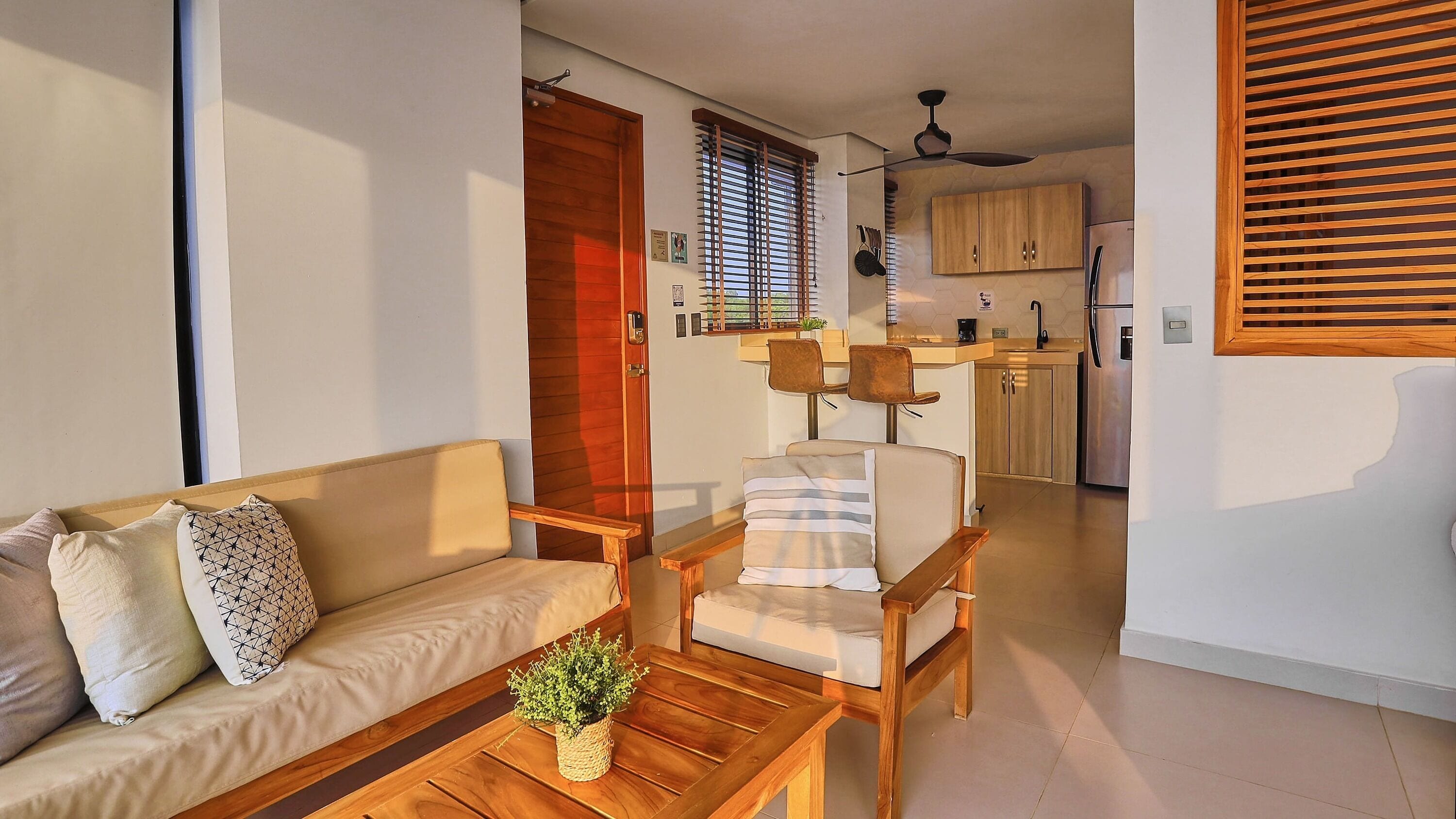 A living room with a sofa, two armchairs, a coffee table with a plant, and a kitchen in the background.