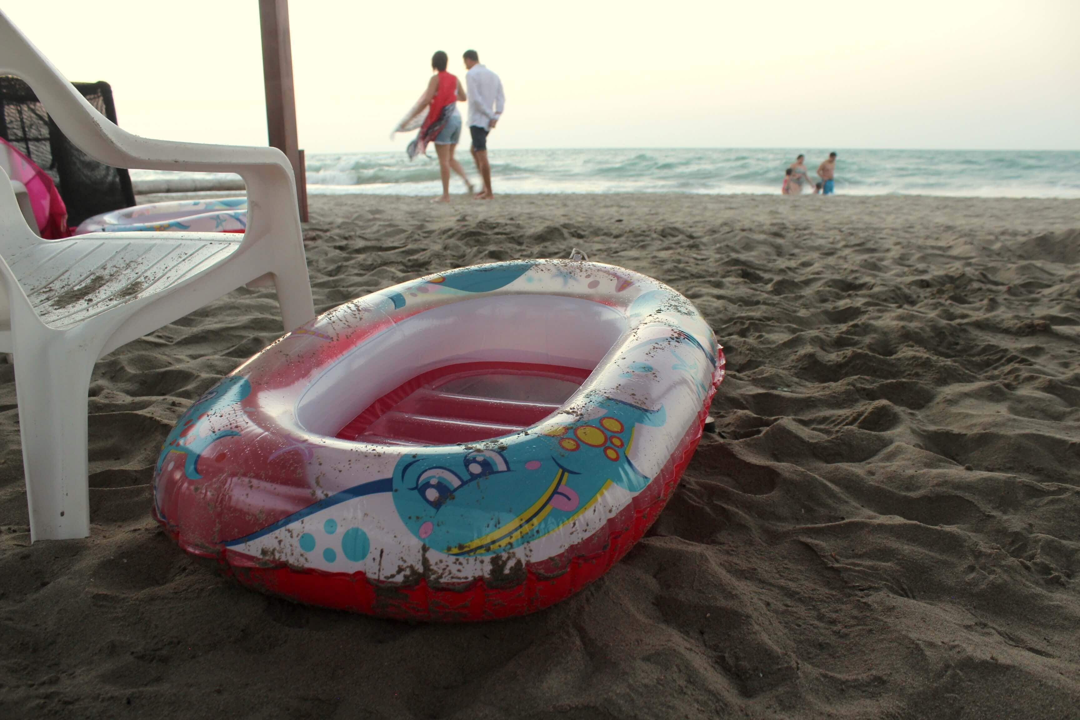 A beach with a colorful inflatable pool and a white plastic chair.