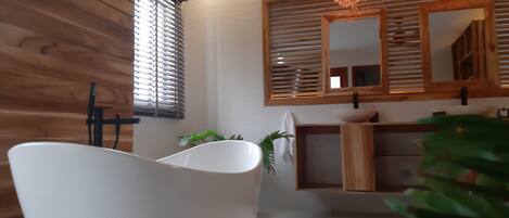 Un baño moderno con una bañera independiente, paneles de madera en la pared, un espejo grande y una lámpara colgante.