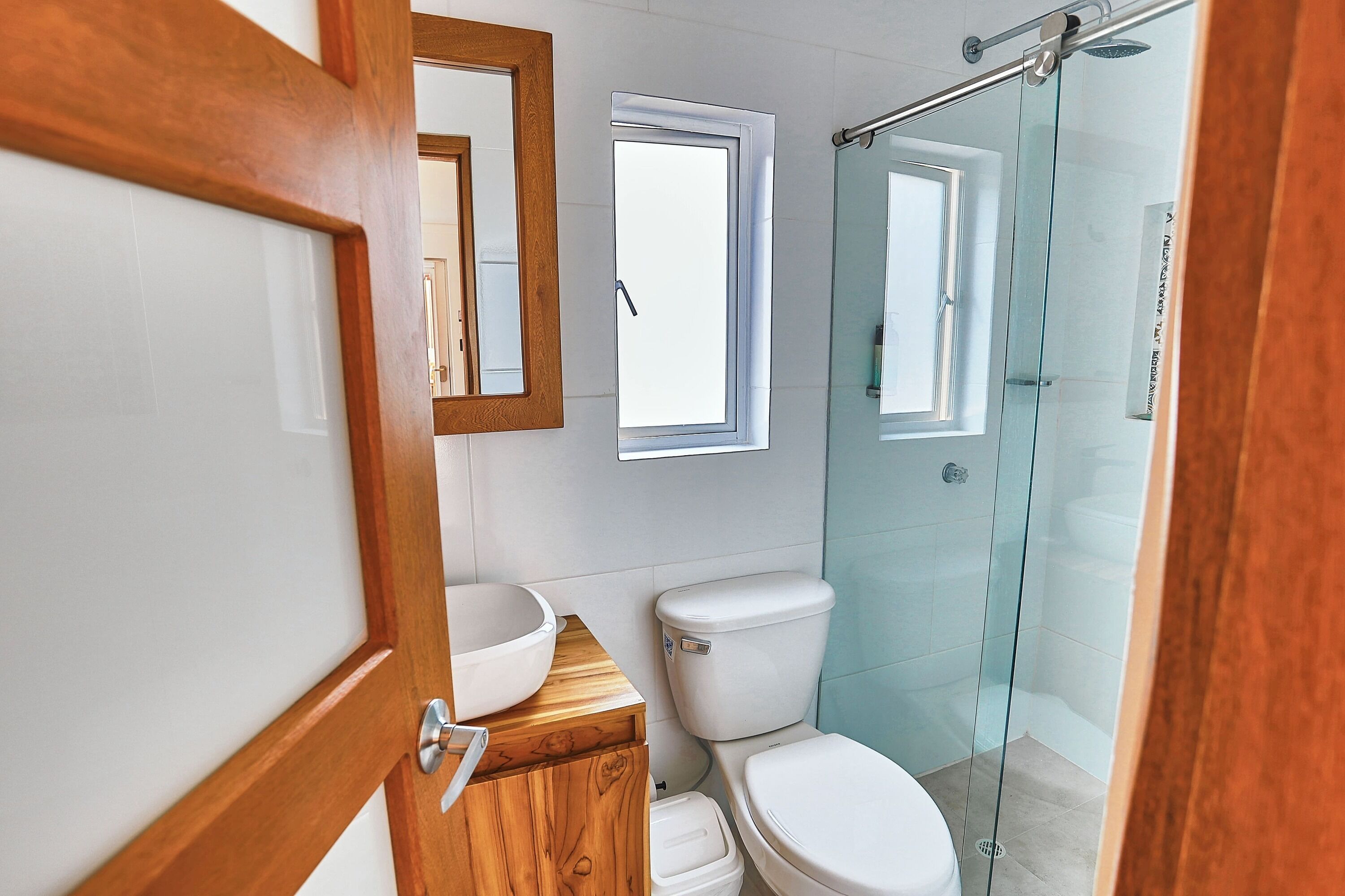 A modern bathroom with a wooden vanity, a toilet, and a glass shower enclosure.