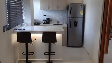 Una cocina moderna con una isla central, dos taburetes de bar, un refrigerador y un ventilador de techo.