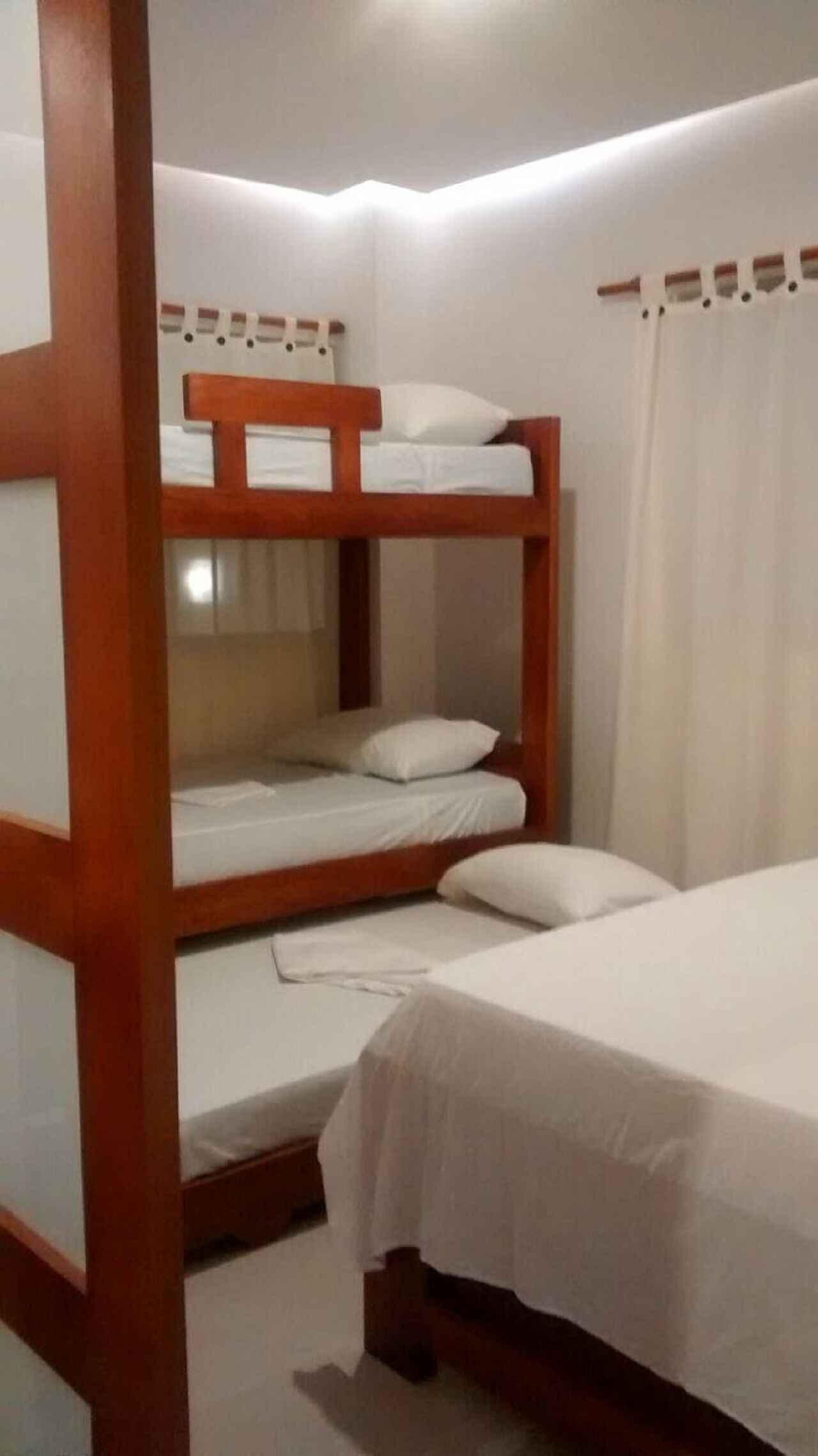 A bunk bed room with a wooden frame, white bedding, and a curtain on the window.