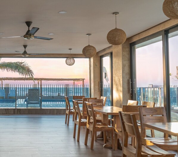 A spacious balcony with wooden furniture, large windows, and a view of the sea at sunset. - Hotel Camino Palmero Coveñas (Coveñas)