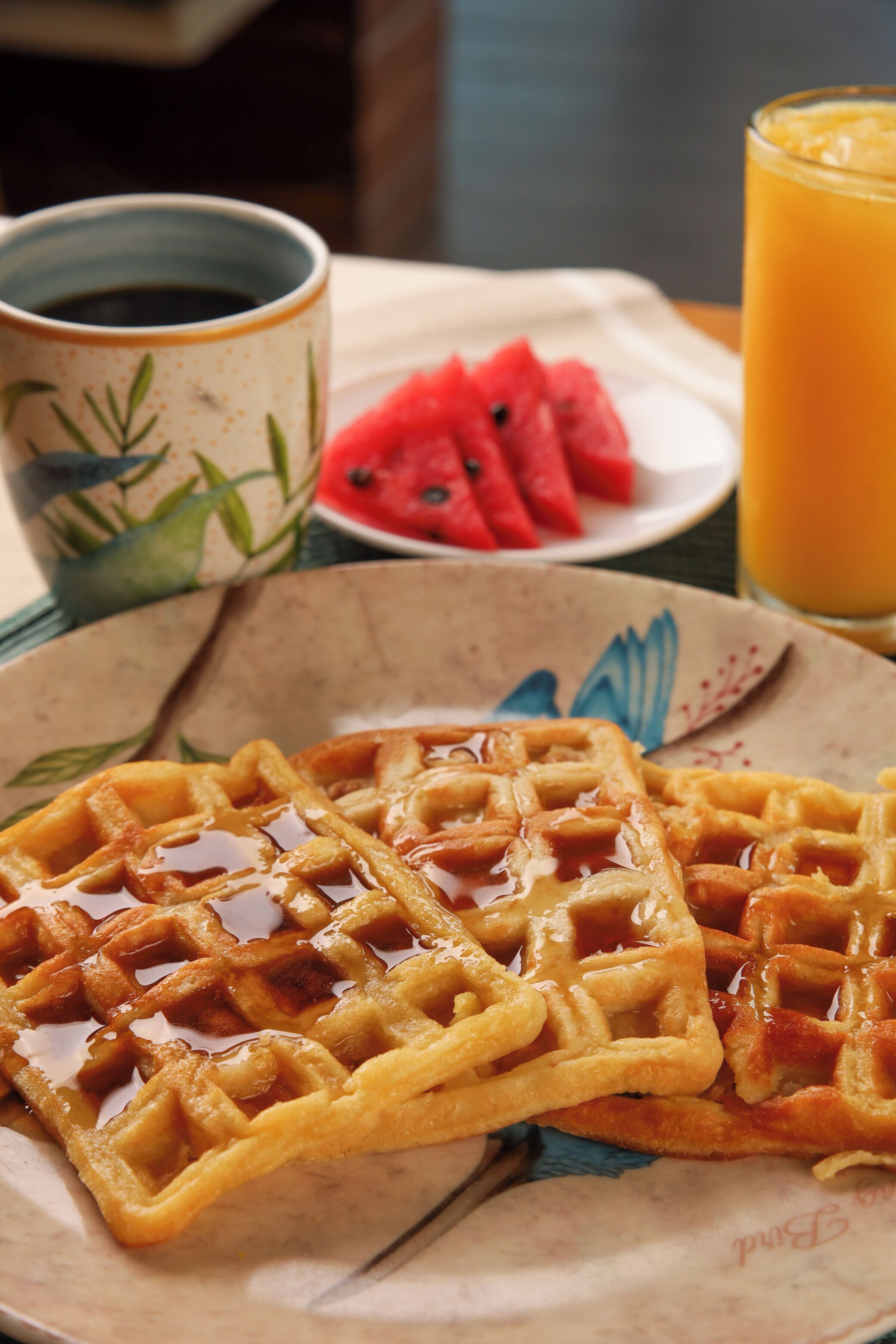 Um prato de waffles com calda, um copo de suco de laranja e uma xícara de café sobre uma mesa.