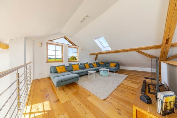 A loft-style room with a wooden floor, a sectional sofa, a round coffee table, and a TV stand.