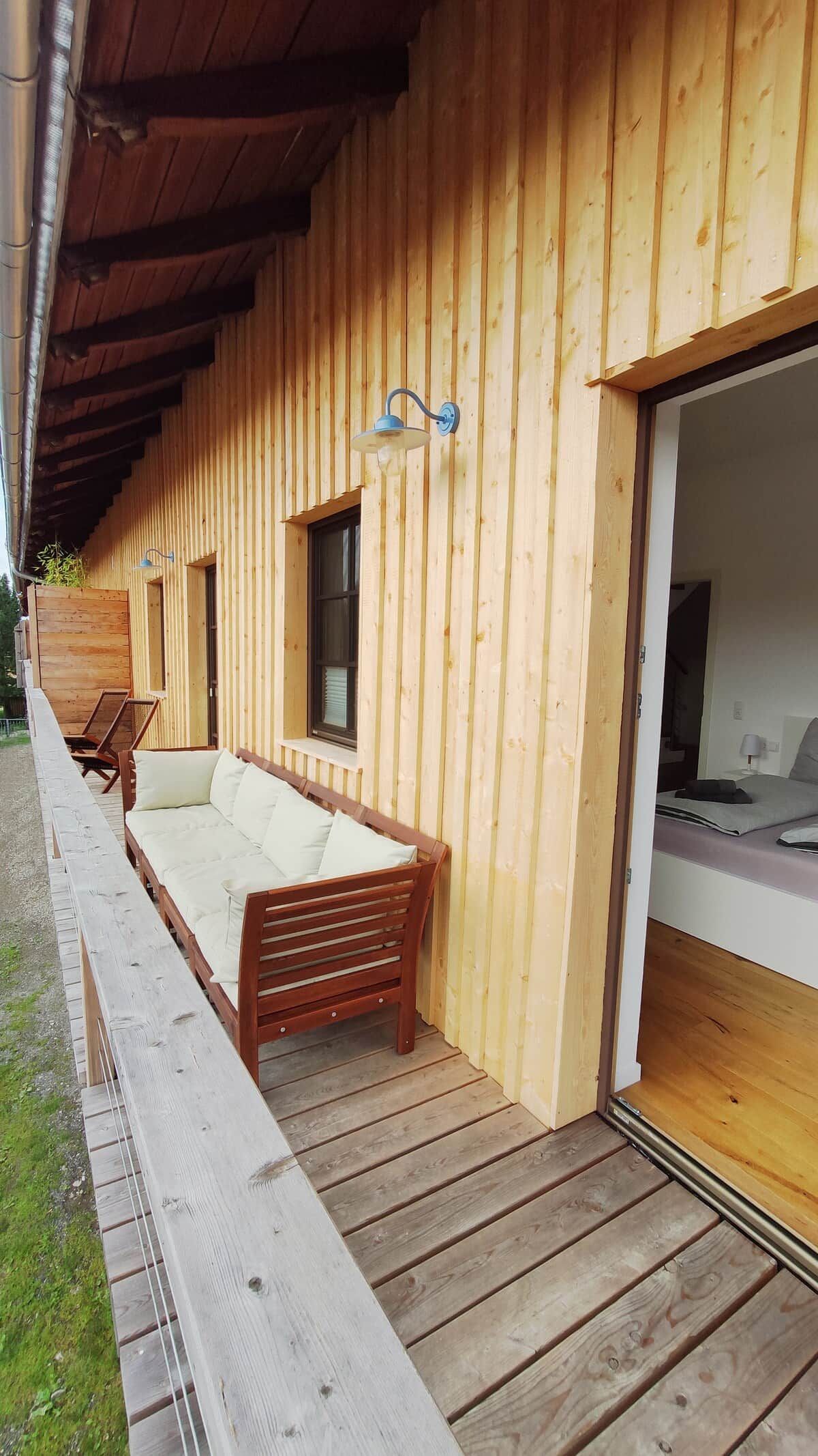 Een houten blokhut met een overdekte veranda, een bank en een bed.