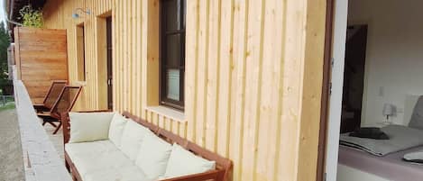 A wooden cabin with a covered porch, a sofa, and a bed.