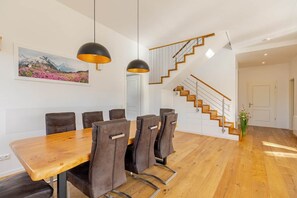 Ein Essbereich mit Holztisch und -stühlen, einer Holztreppe und Pendelleuchten.