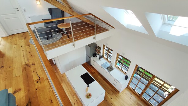 Un espacioso apartamento estilo loft con piso de madera, un entrepiso con zona de estar, una cocina con nevera empotrada y ventanas amplias que ofrecen vistas.