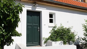 Um edifício branco com porta verde, uma janela pequena e telhado em telhas.
