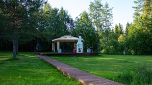 A wooden deck leading to a gazebo with a chimney, surrounded by lush greenery.