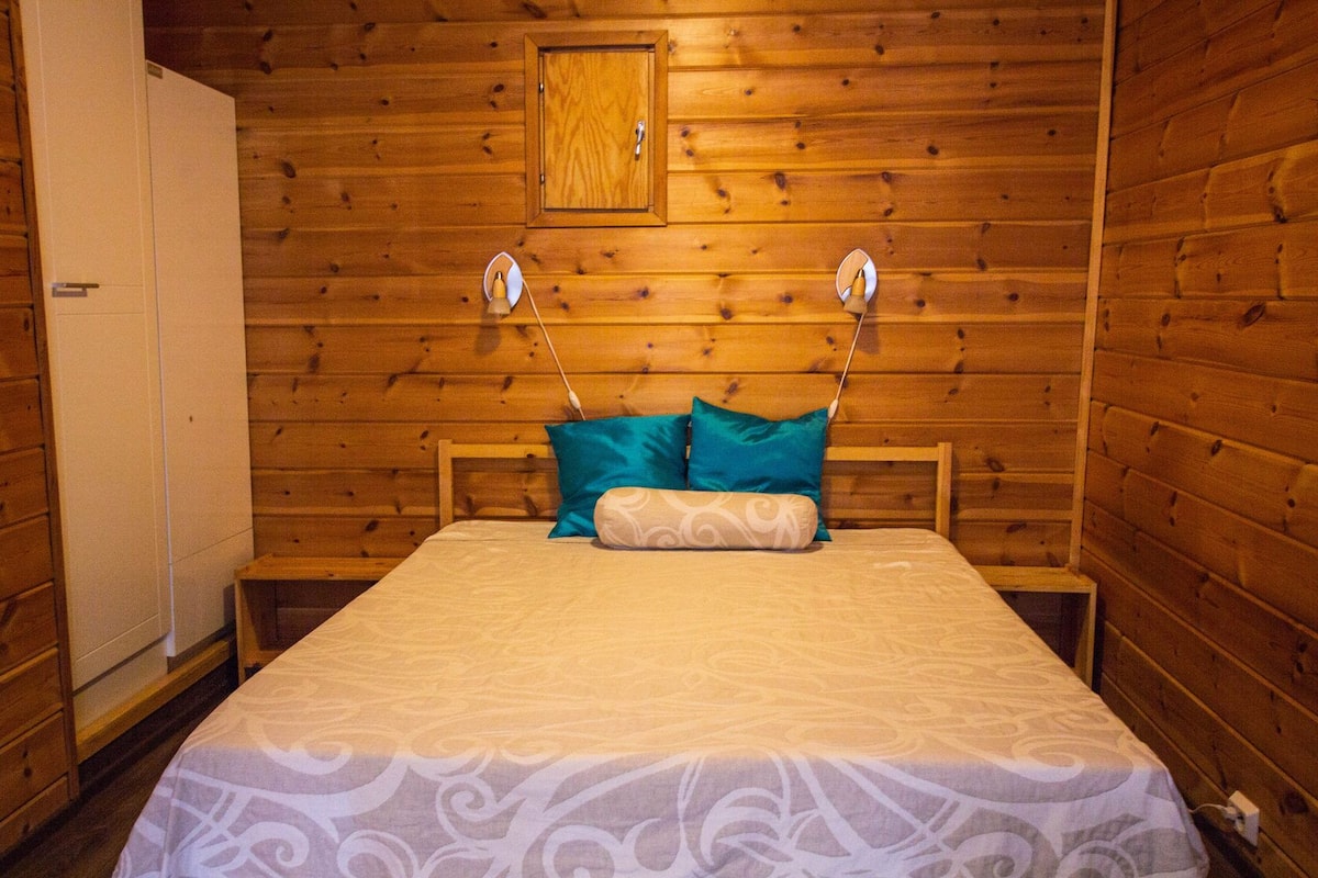 A wooden-paneled room with a bed, a wardrobe, and a small cabinet.
