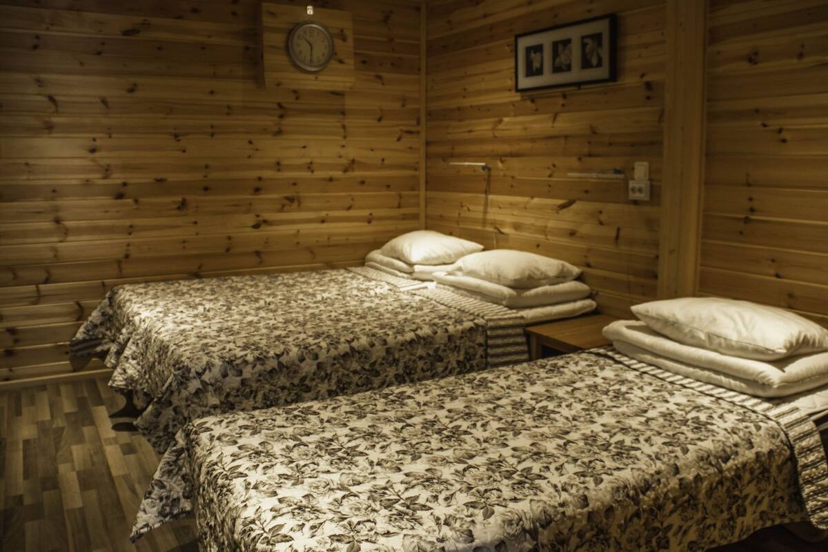 A wooden cabin room with two beds, each with floral bedding and pillows, a wooden wall clock, and a framed picture above the beds.