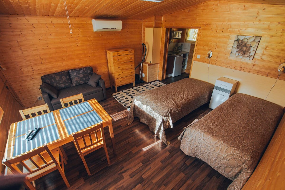 A cozy cabin with two beds, a dining table, a sofa, a kitchen area, and a built-in air conditioning unit.
