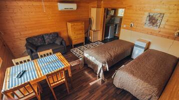A cozy cabin with two beds, a dining table, a sofa, a kitchen area, and a built-in air conditioning unit.