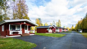 A row of red cabins with white trim, a paved driveway, and a grassy area.