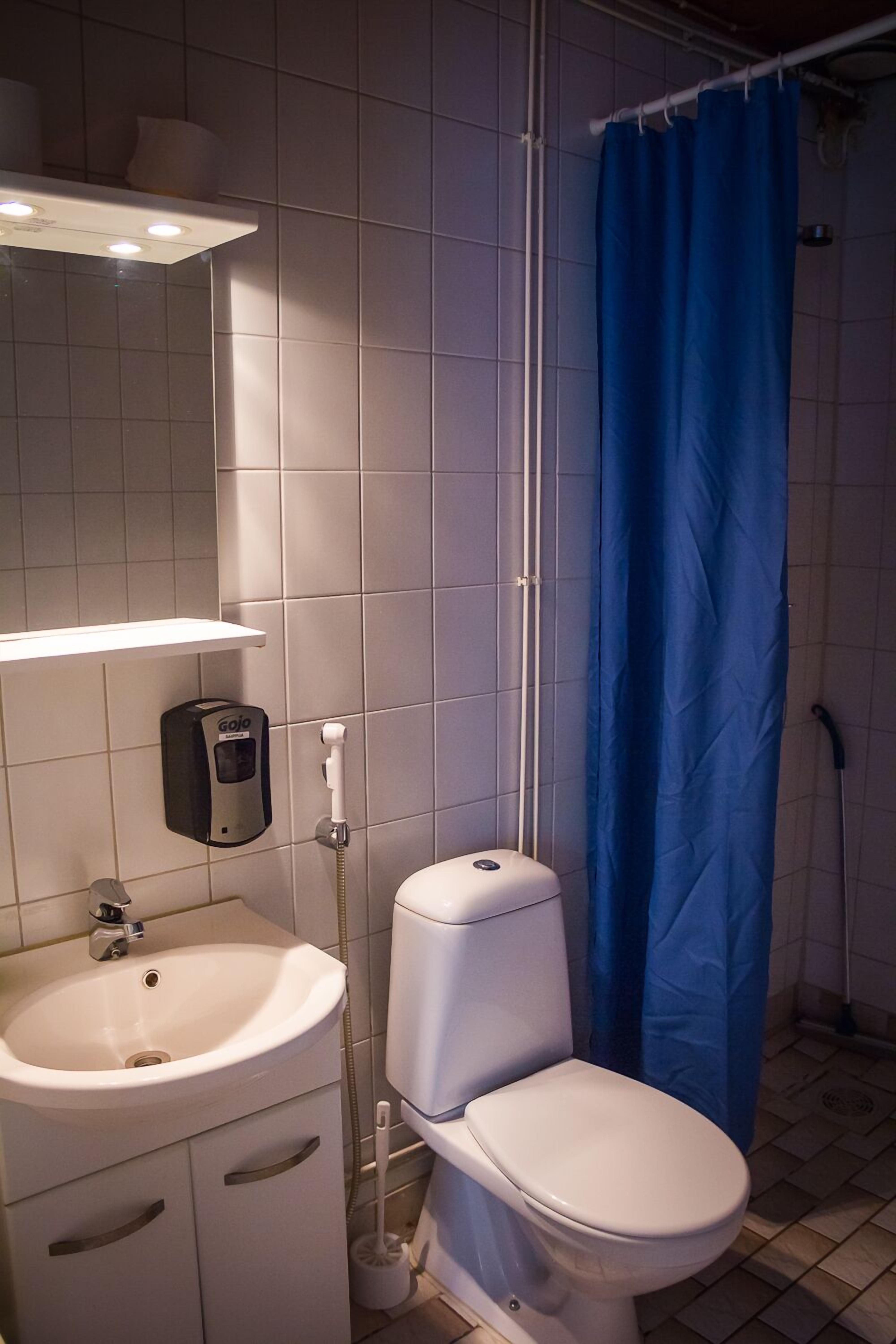 A bathroom with a white sink, a toilet, a blue shower curtain, and a hand dryer.