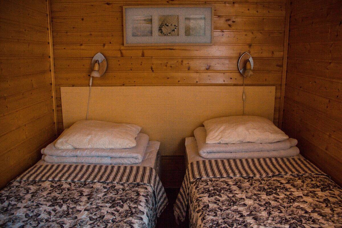 A room with two beds, each with a floral-patterned bedspread and a striped pillow. There is a framed picture on the wall above the beds.