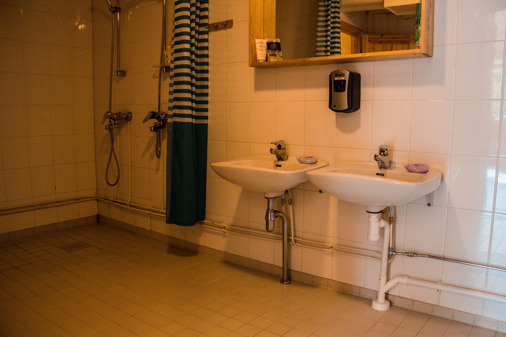A bathroom with a shower, two sinks, a towel rack, and a soap dispenser.