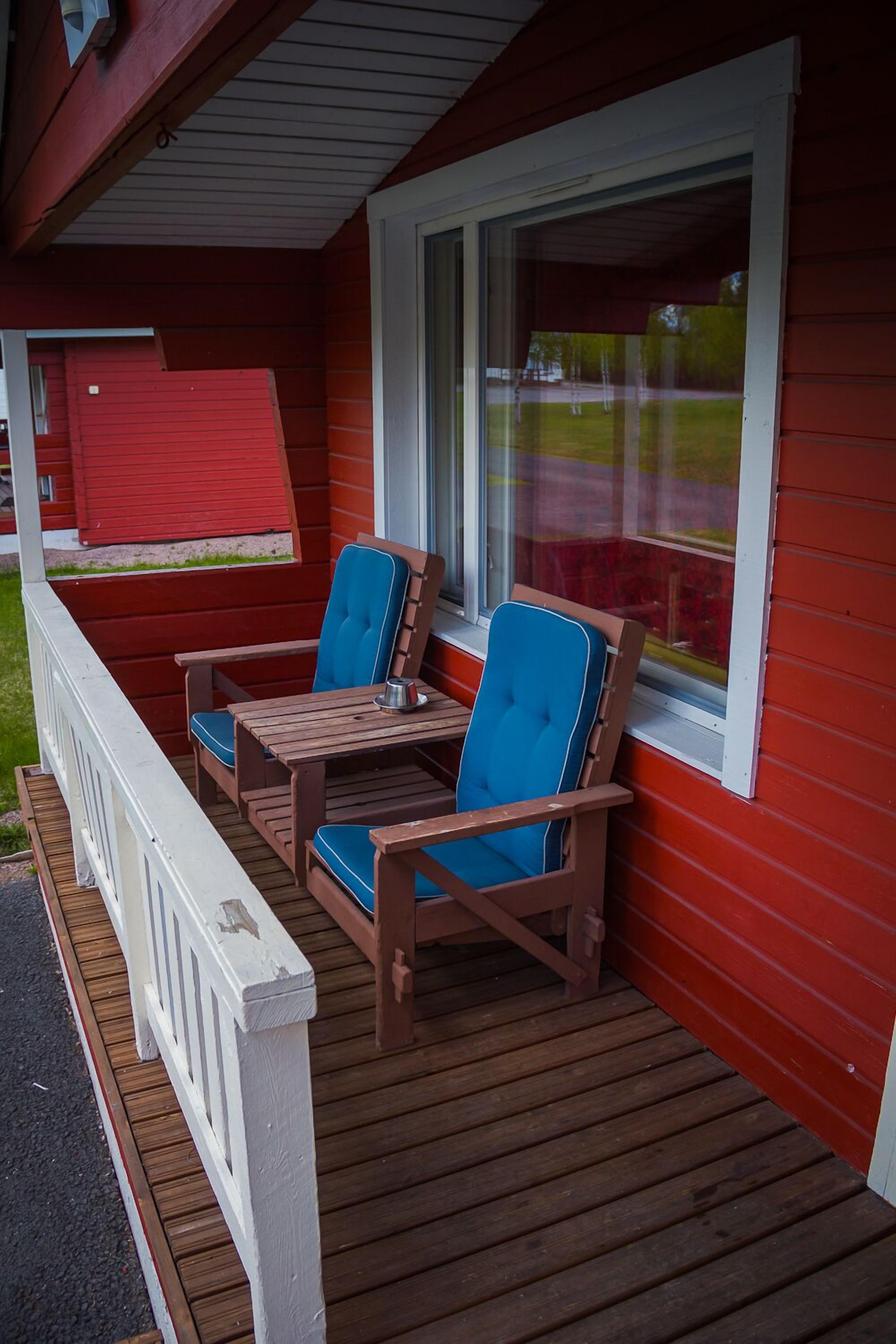 Terraza de madera con dos sillas azules acolchadas y una mesita.