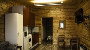 A compact kitchen with a refrigerator, microwave, stove, and sink. There is a wooden dining table with chairs, a sofa, and a television mounted on the wall.
