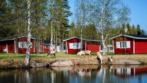 Un área de cabañas junto al lago, con cabañas rojas, un lago tranquilo y un fondo boscoso.