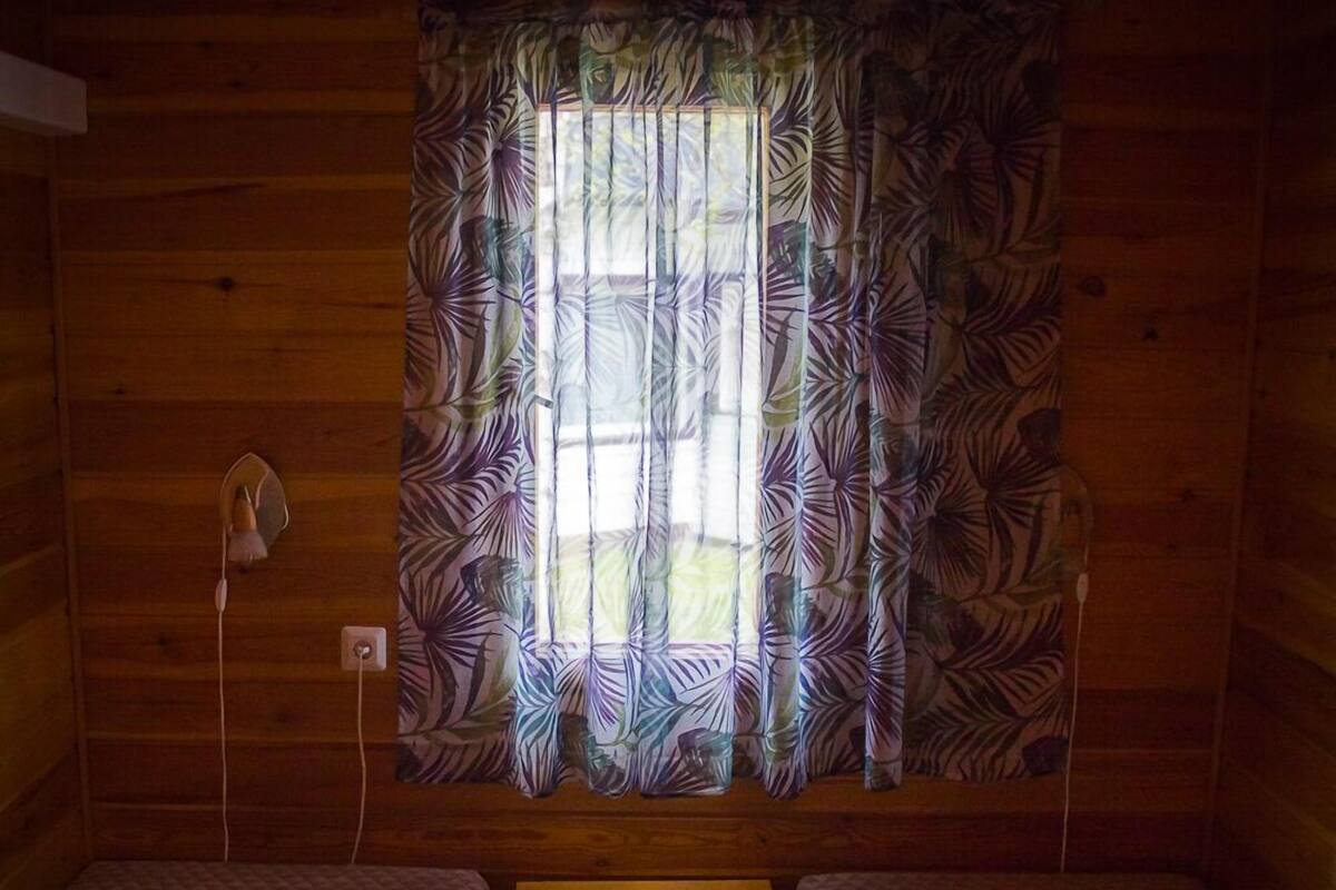 A cabin with two single beds, a small table, and a window with patterned curtains.