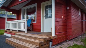 A red wooden house with a white door and a blue chair on the porch.