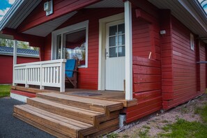 A red wooden house with a white door and a blue chair on the porch.