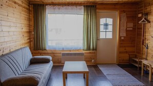 Interior acogedor de una cabaña con sofá, una mesita, un calentador y una ventana con cortinas.