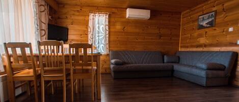 A wooden interior with a dining table and chairs, a sofa, and an air conditioning unit.