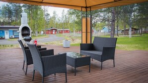 Un patio exterior con mobiliario de mimbre, una parrilla y un espacio cubierto.