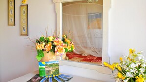 Una habitació amb un llit, una finestra amb un cortinat lleuger, un ram de flors i quadres a la paret.