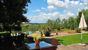 Zona d'seients a l'aire lliure amb cadires de vimetla i una taula de vidre, amb vista a un jardí paisatgístic i una piscina.