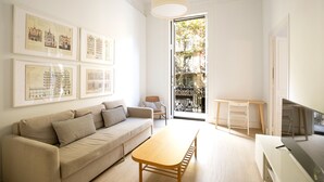 A modern living room with a sofa, coffee table, and a TV. There are framed pictures on the wall and a balcony with a railing. - Stylish apartment, very bright. Located in the center of Barcelona (Barcelona)