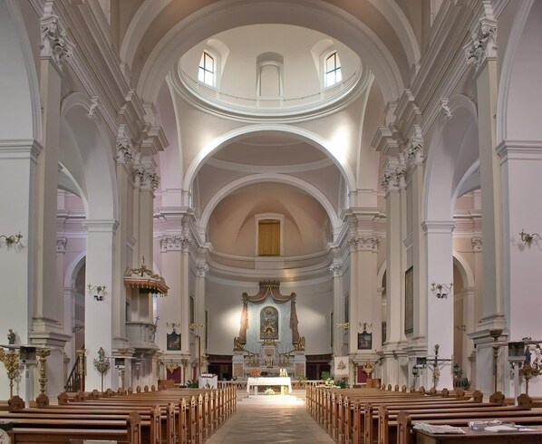 Stunning church interior with a high, arched ceiling and central altar, surrounded by rows of pews and ornate columns.