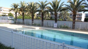 Une piscine entourée d’une clôture blanche, avec des palmiers et un camping-car blanc garé à proximité.