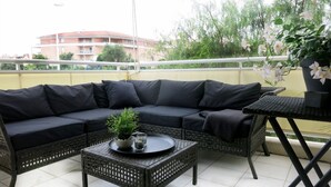 Un balcon avec un canapé noir, une table en osier sur laquelle repose un plateau, et une plante en pot.