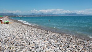 Une plage de galets bordée d’une eau d’un bleu limpide et dominée par des montagnes lointaines.