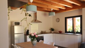 A modern kitchen with white cabinets, a wooden dining table, and hanging pendant lights.
