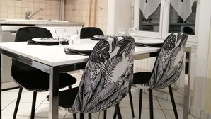 Un comedor con una mesa blanca, sillas negras con motivos de hojas, una ventana con cortinas blanco y negro, y un salpicadero de azulejos.