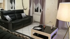 Una sala de estar con un sofá negro, una mesa de centro de vidrio y una lámpara.