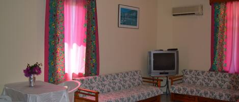 Una sala de estar con un sofá, un televisor, una mesa con un florero y cortinas con estampado floral.