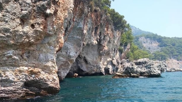 Three people swimming in a clear blue sea with rocky cliffs in the background.