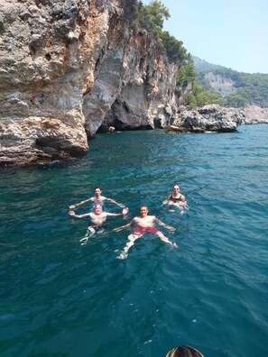 Three people swimming in a clear blue sea with rocky cliffs in the background. - Erasmus Apart Hotel (Ortaca)