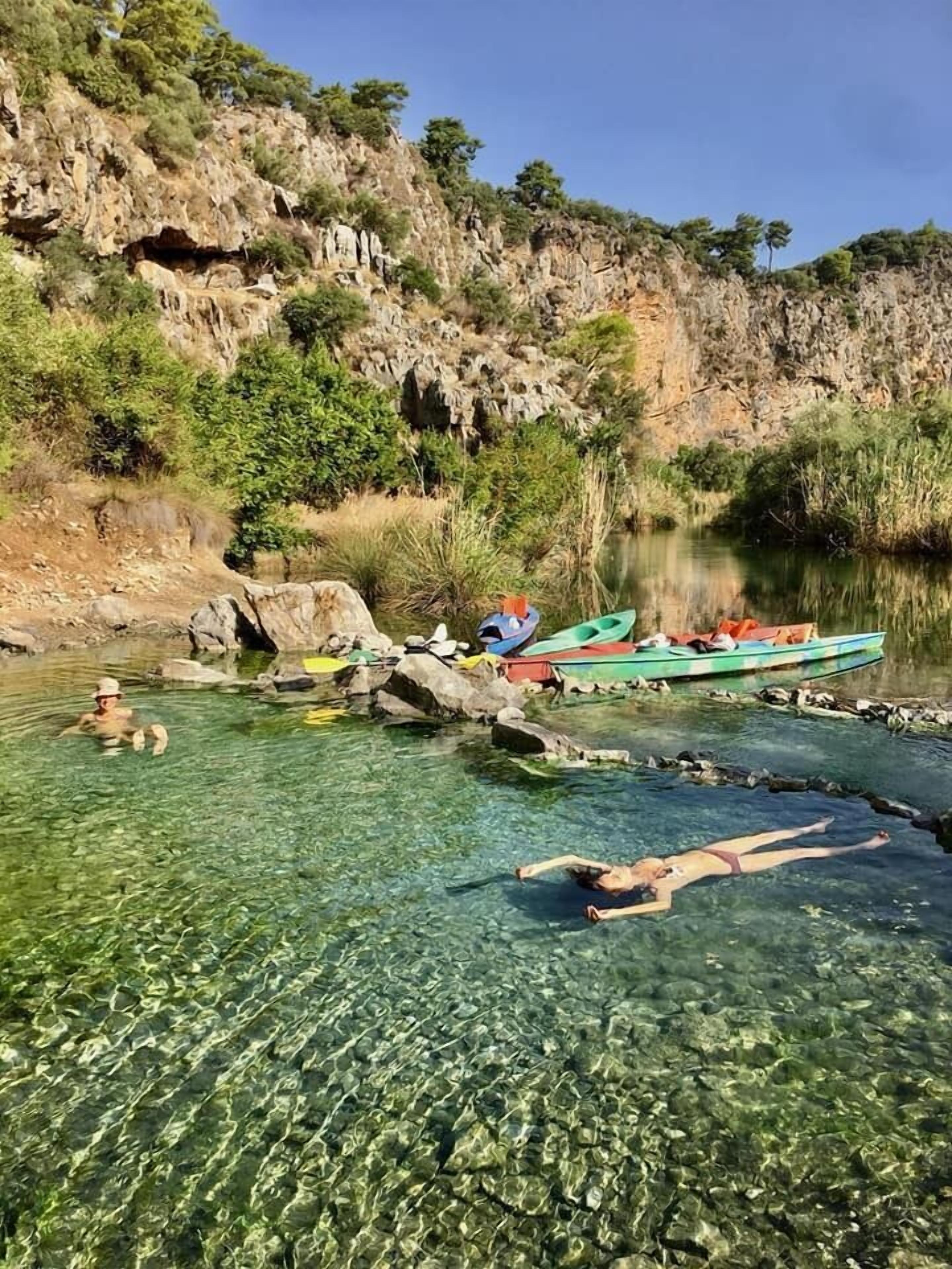 A clear river with people swimming and boats docked.