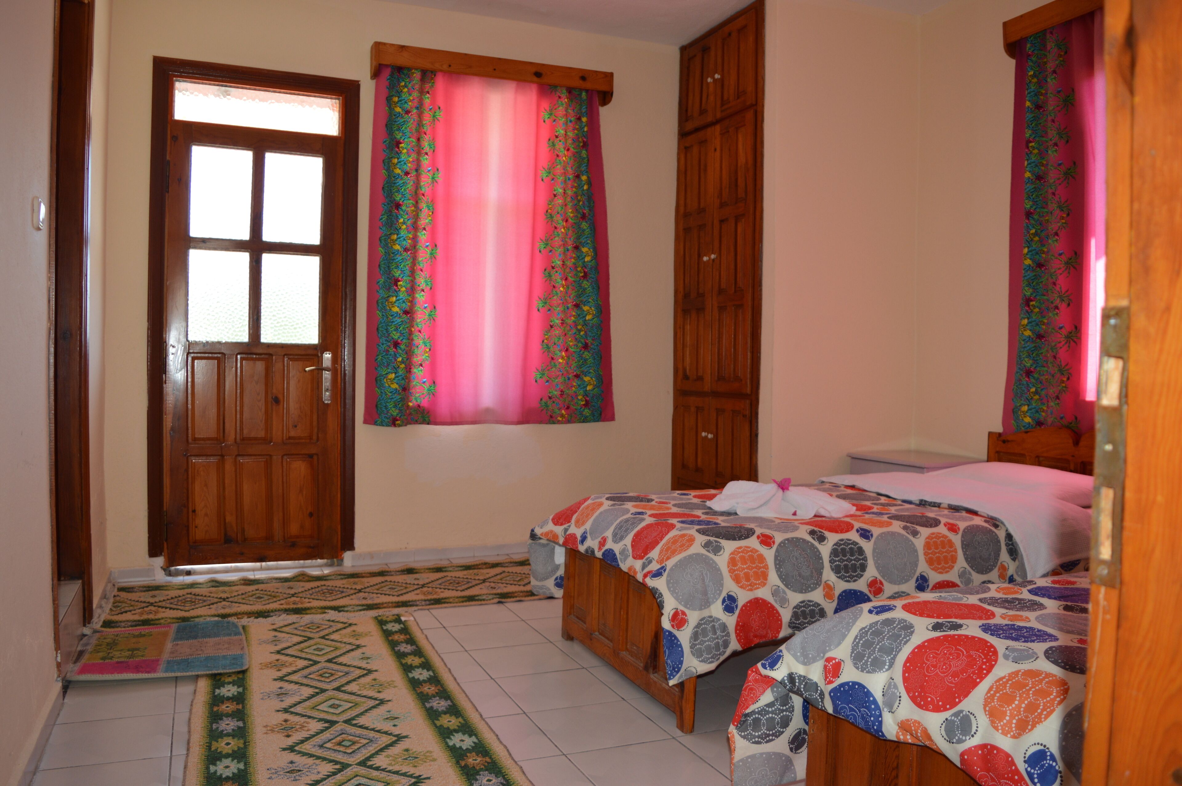 Un dormitorio con dos camas, un armario de madera, una puerta con ventanal y una alfombra estampada.